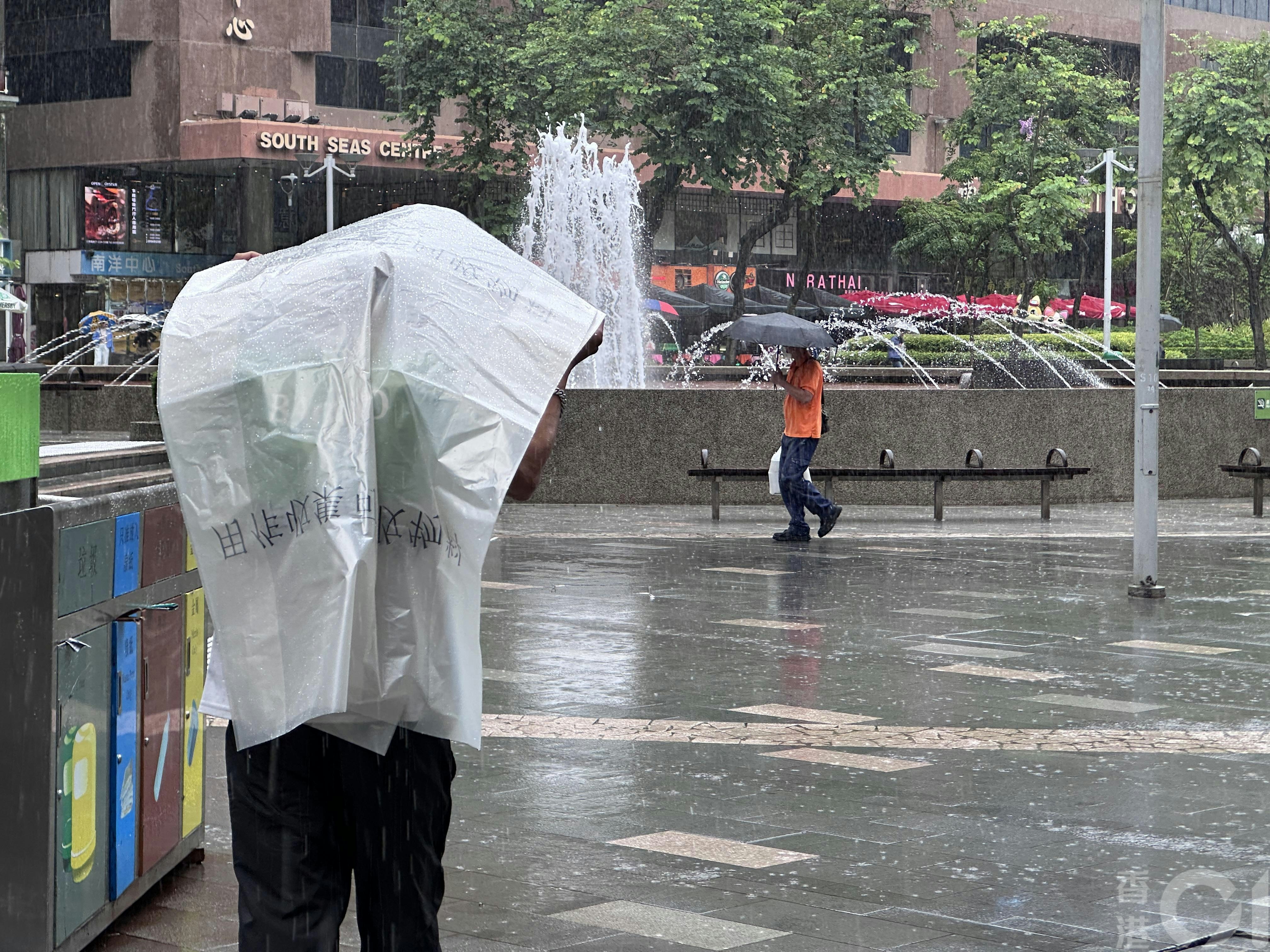 7月16日中午时分尖东忽然下大雨,有食环署外判工人拿垃圾袋暂当雨衣遮身。(倪清江摄)